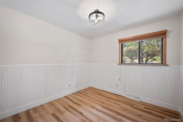 empty room with wainscoting, wood finished floors, and visible vents