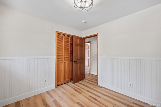 unfurnished bedroom featuring a closet, wainscoting, and light wood-style flooring