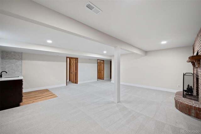 basement featuring light colored carpet and a brick fireplace