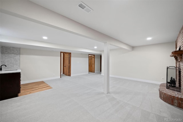 finished below grade area featuring light colored carpet, recessed lighting, a brick fireplace, and visible vents