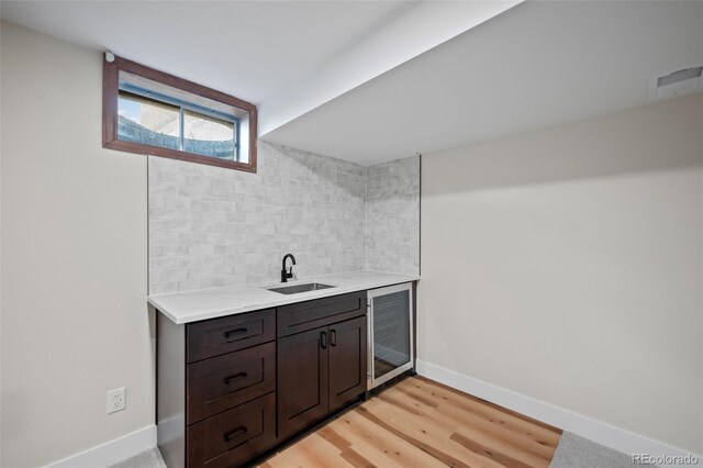 bar with wine cooler, tasteful backsplash, light hardwood / wood-style floors, sink, and dark brown cabinetry