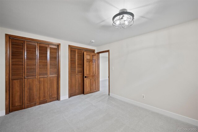 unfurnished bedroom featuring light colored carpet and multiple closets