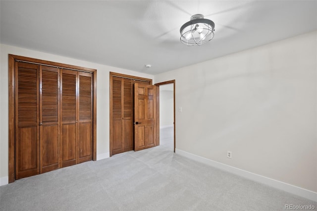 unfurnished bedroom with baseboards, light colored carpet, and multiple closets