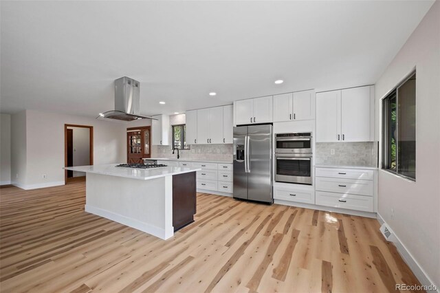 kitchen featuring island range hood, light hardwood / wood-style flooring, appliances with stainless steel finishes, and white cabinets