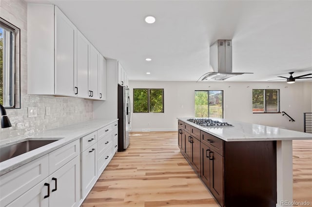 kitchen with appliances with stainless steel finishes, light hardwood / wood-style floors, dark brown cabinets, a kitchen island, and island range hood