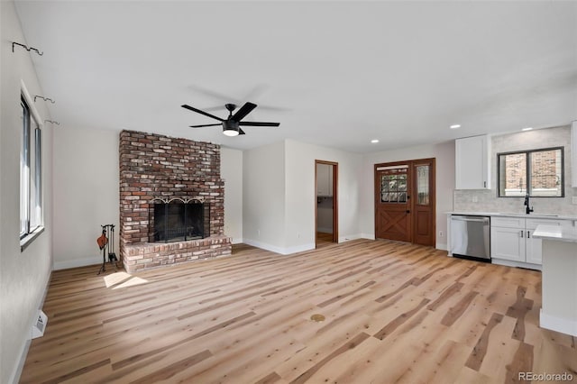 unfurnished living room with a fireplace, ceiling fan, sink, and light hardwood / wood-style floors