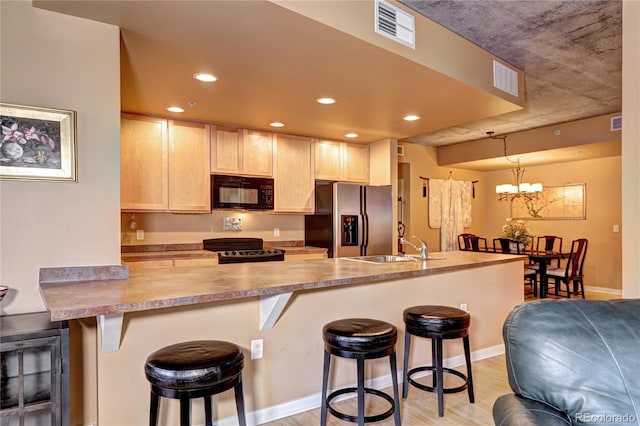 kitchen featuring black appliances, light hardwood / wood-style floors, an inviting chandelier, and a kitchen bar