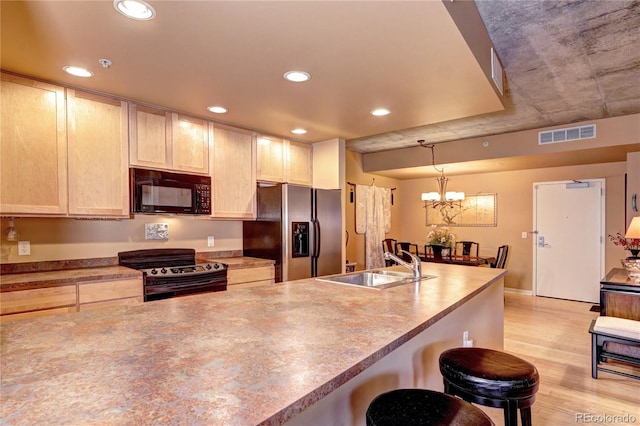 kitchen with pendant lighting, a chandelier, light hardwood / wood-style floors, sink, and black appliances