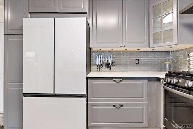 kitchen with white refrigerator, gas range, gray cabinetry, and decorative backsplash