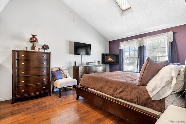 bedroom with vaulted ceiling with skylight, hardwood / wood-style floors, and a textured ceiling