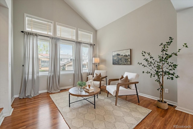 living area featuring wood finished floors, high vaulted ceiling, and baseboards