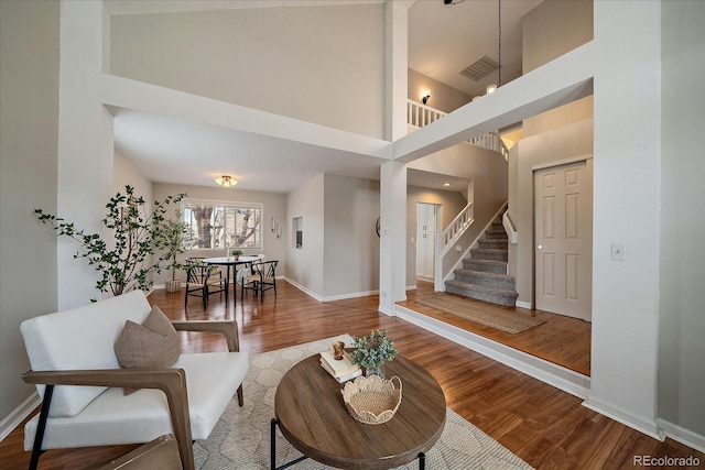 living area featuring baseboards, wood finished floors, stairway, and a towering ceiling