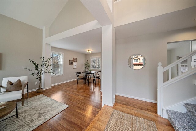 foyer with stairs, wood finished floors, baseboards, and high vaulted ceiling