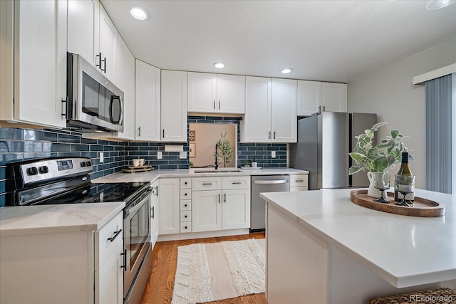 kitchen featuring stainless steel appliances, light wood finished floors, a sink, white cabinetry, and backsplash