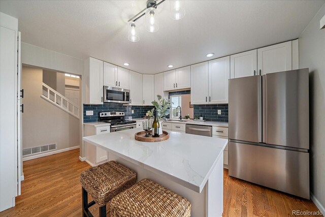 kitchen with appliances with stainless steel finishes, a sink, light wood-style flooring, white cabinets, and recessed lighting