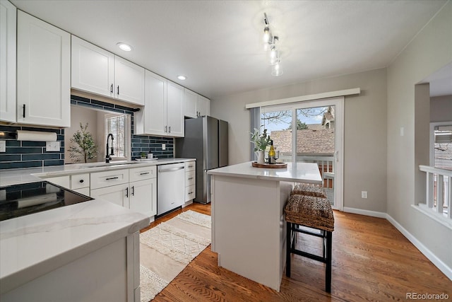 kitchen featuring stainless steel appliances, a sink, backsplash, white cabinetry, and light wood-type flooring