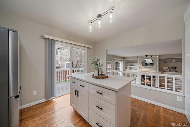 kitchen with freestanding refrigerator, white cabinets, baseboards, a kitchen island, and light wood-type flooring