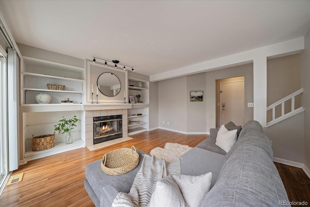 living room featuring wood finished floors, a fireplace, baseboards, and built in features