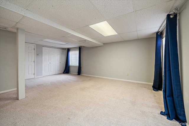 basement with carpet floors, a paneled ceiling, and baseboards