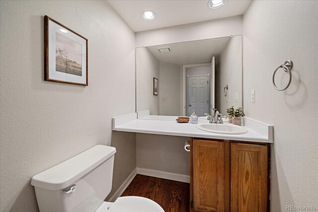 half bath featuring wood finished floors, toilet, vanity, baseboards, and recessed lighting