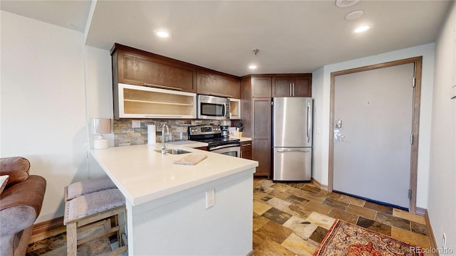 kitchen featuring dark brown cabinetry, sink, kitchen peninsula, appliances with stainless steel finishes, and backsplash