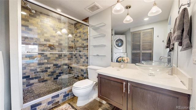 bathroom with vanity, a shower with shower door, stacked washing maching and dryer, tile patterned floors, and toilet