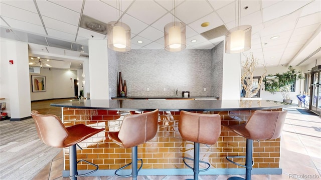 bar featuring tile patterned flooring, a drop ceiling, tasteful backsplash, and sink