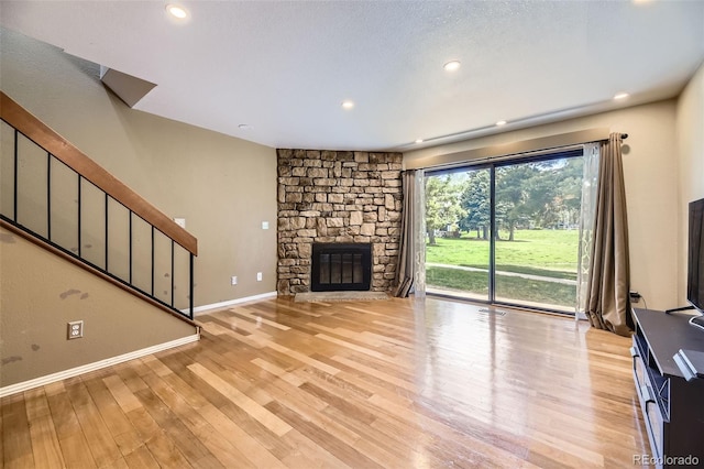 unfurnished living room featuring recessed lighting, stairway, a fireplace, baseboards, and light wood-style floors