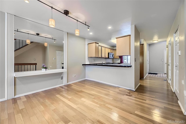 kitchen with baseboards, light wood finished floors, stainless steel microwave, rail lighting, and dark countertops