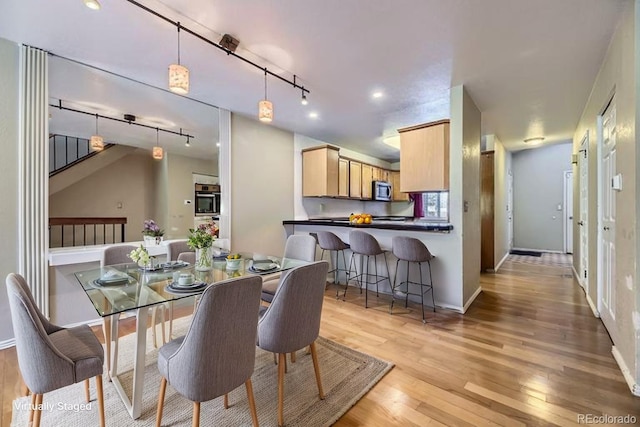dining room featuring track lighting, light wood finished floors, and baseboards