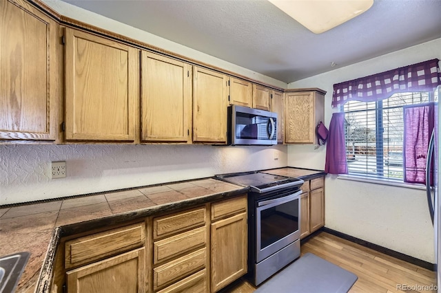 kitchen featuring tile countertops, light wood-style flooring, baseboards, and appliances with stainless steel finishes