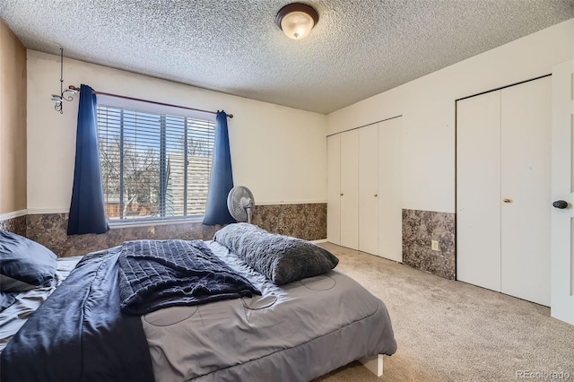 carpeted bedroom featuring a textured ceiling, two closets, and a wainscoted wall