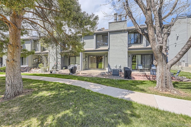 rear view of property with central air condition unit, a patio area, a chimney, and a lawn