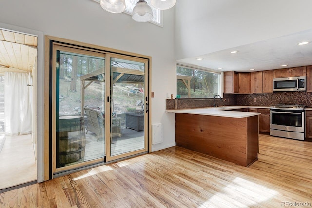8795 Rudd Rd, Evergreen, CO 80439 - kitchen featuring appliances with stainless steel finishes, light wood-type flooring, a peninsula, brown cabinetry, and a towering ceiling