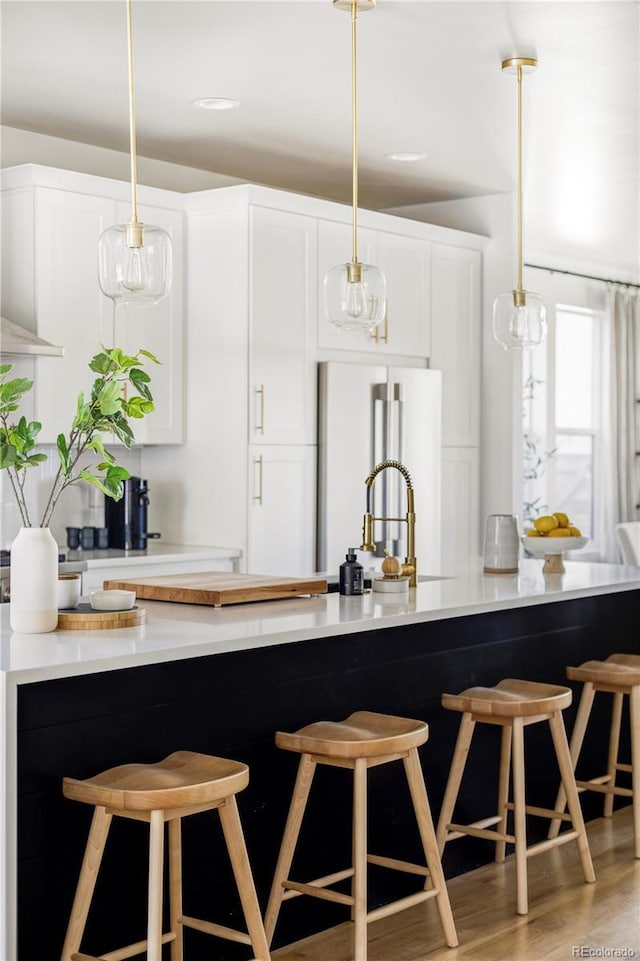 kitchen featuring a kitchen bar, white cabinetry, hanging light fixtures, light hardwood / wood-style flooring, and high end refrigerator