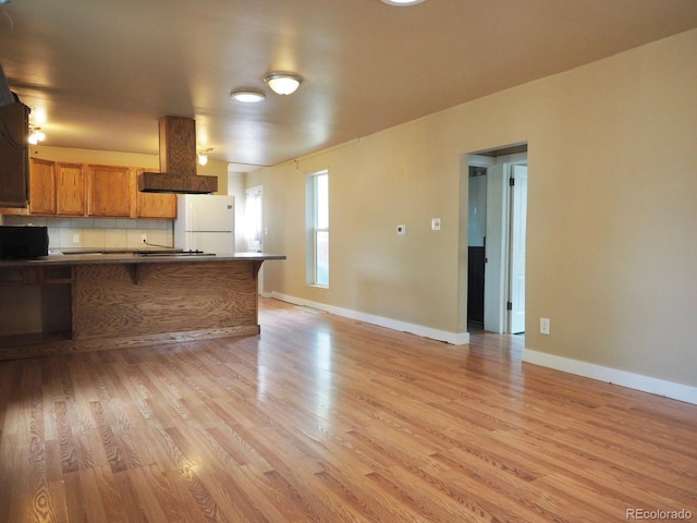 kitchen with freestanding refrigerator, brown cabinetry, dark countertops, and light wood-type flooring
