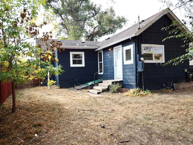 back of house with entry steps, fence, and a shingled roof