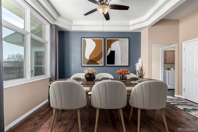 dining area featuring dark wood-type flooring, washing machine and clothes dryer, a tray ceiling, and ceiling fan