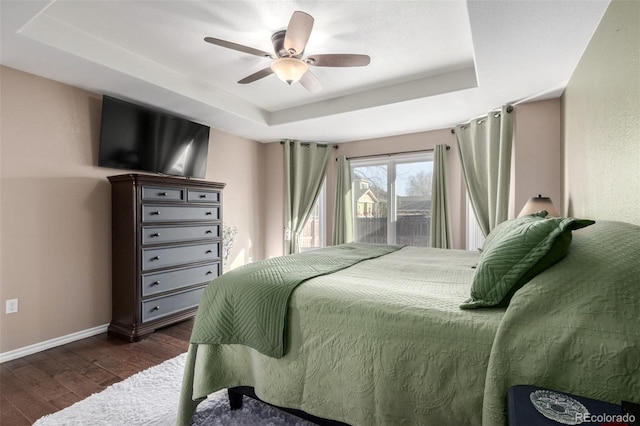 bedroom featuring ceiling fan, access to exterior, dark hardwood / wood-style flooring, and a tray ceiling