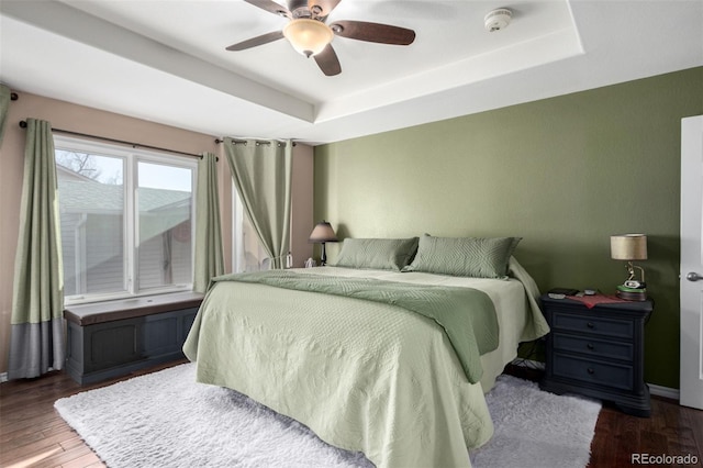 bedroom with ceiling fan, a tray ceiling, and dark hardwood / wood-style flooring