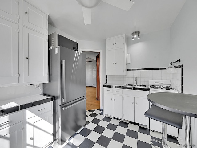 kitchen featuring a sink, dark floors, freestanding refrigerator, tile countertops, and white cabinetry