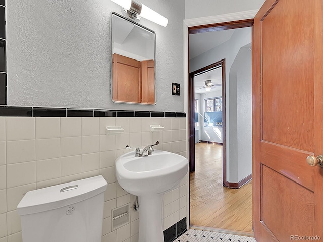 bathroom with a ceiling fan, tile walls, toilet, wainscoting, and a textured wall
