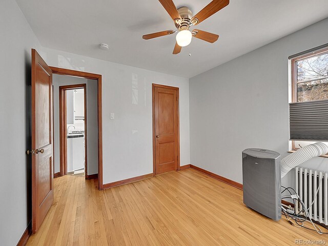 spare room with light wood-style floors, baseboards, ceiling fan, and radiator heating unit