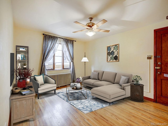 living room featuring light wood-style flooring, baseboards, ceiling fan, and radiator heating unit