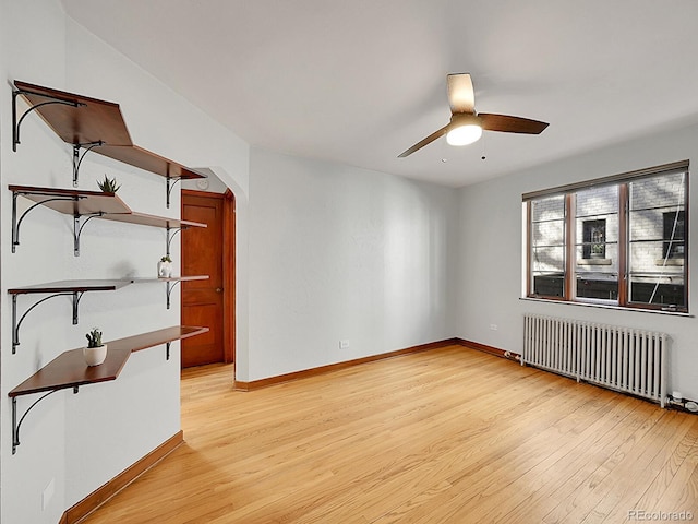unfurnished room with radiator, light wood-type flooring, a ceiling fan, arched walkways, and baseboards