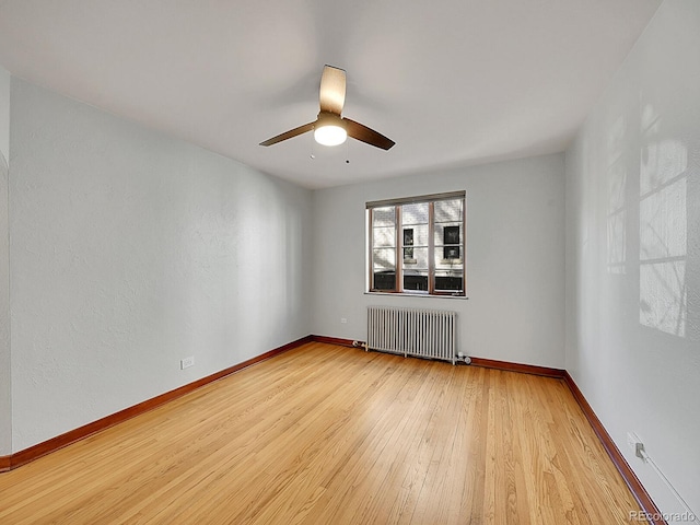 empty room with radiator heating unit, wood finished floors, ceiling fan, and baseboards