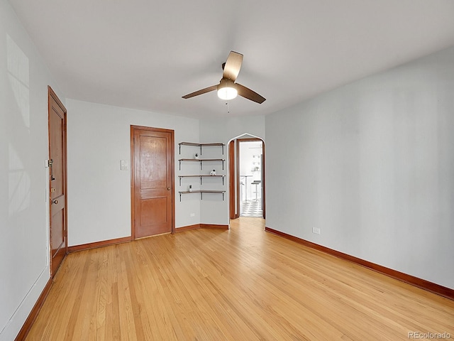 empty room featuring baseboards, light wood-style flooring, a ceiling fan, and arched walkways