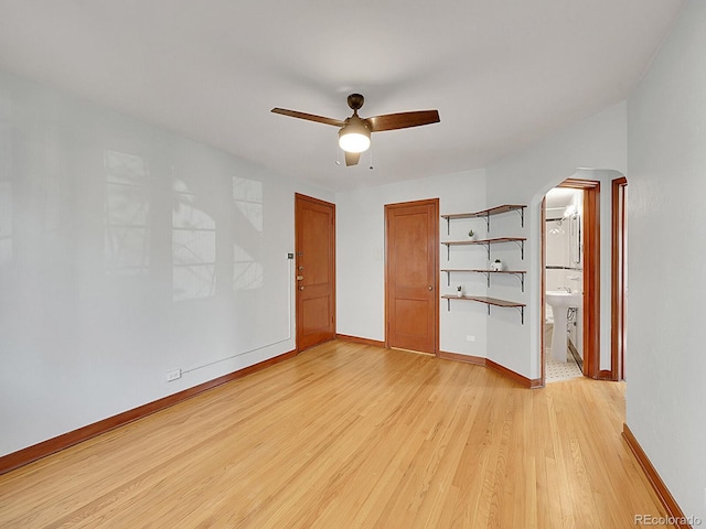 unfurnished room featuring ceiling fan, arched walkways, baseboards, and light wood-style floors