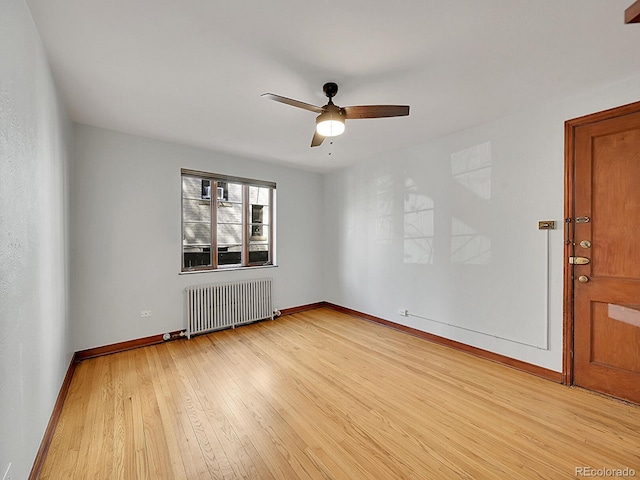 empty room with ceiling fan, radiator, baseboards, and light wood-style floors
