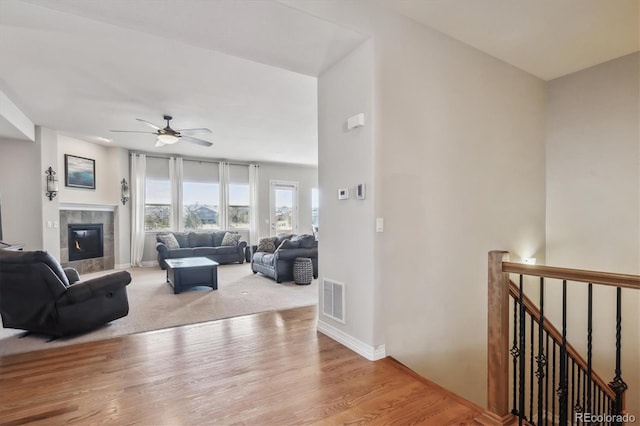 living room with visible vents, ceiling fan, baseboards, a tile fireplace, and wood finished floors